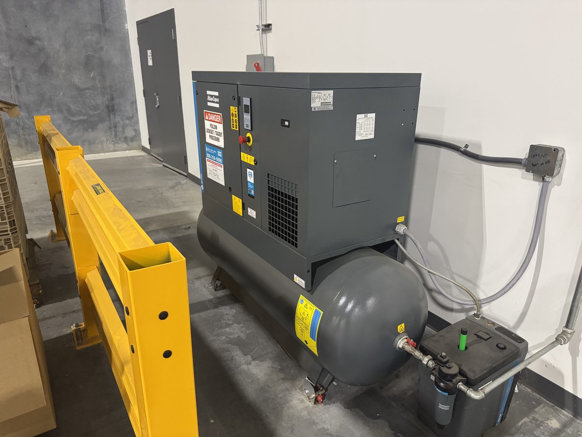 Rotary screw compressor with receiver tank behind machine guarding