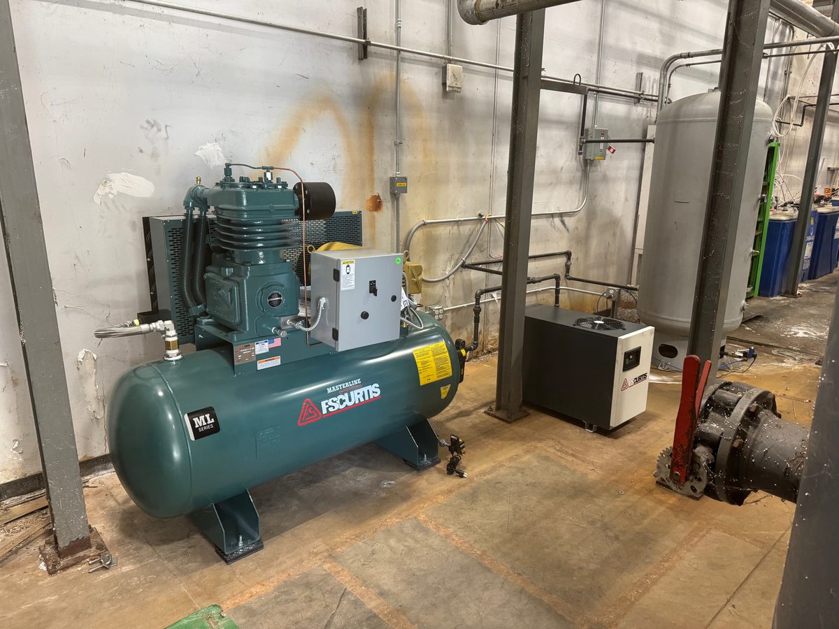 Older reciprocating air compressor with horizontal receiver tank in a plant
