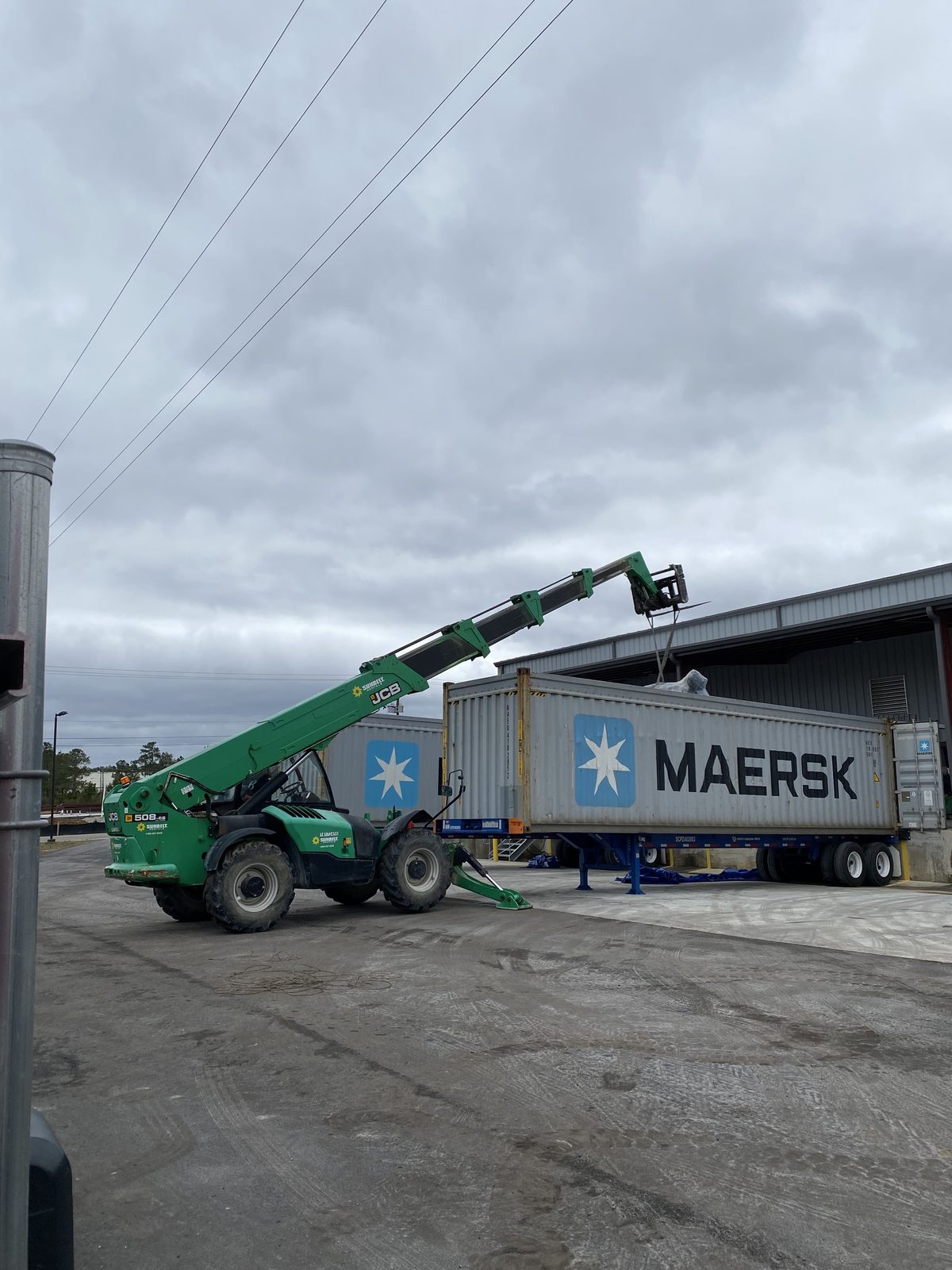 Telehandler positioning equipment beside a shipping container at an industrial yard